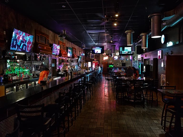 A dimly lit modern bar interior featuring a long counter and multiple screens, creating a cozy urban atmosphere. sports b