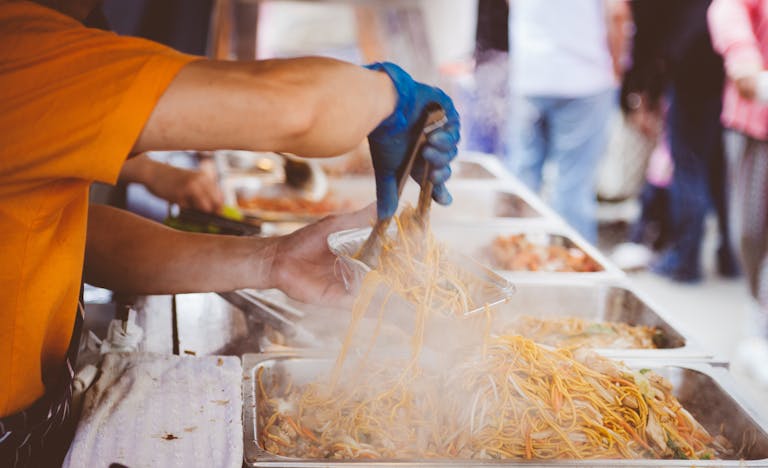 A street vendor serving freshly cooked noodles at a bustling outdoor market. food and drink festivals in atlanta