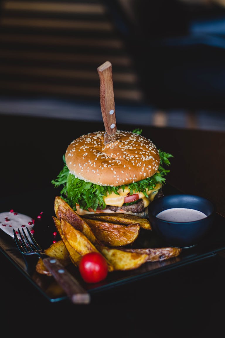 Close-up of a gourmet cheeseburger with wedges and tomato on a black plate. Celebrity restaurants in Atlanta.