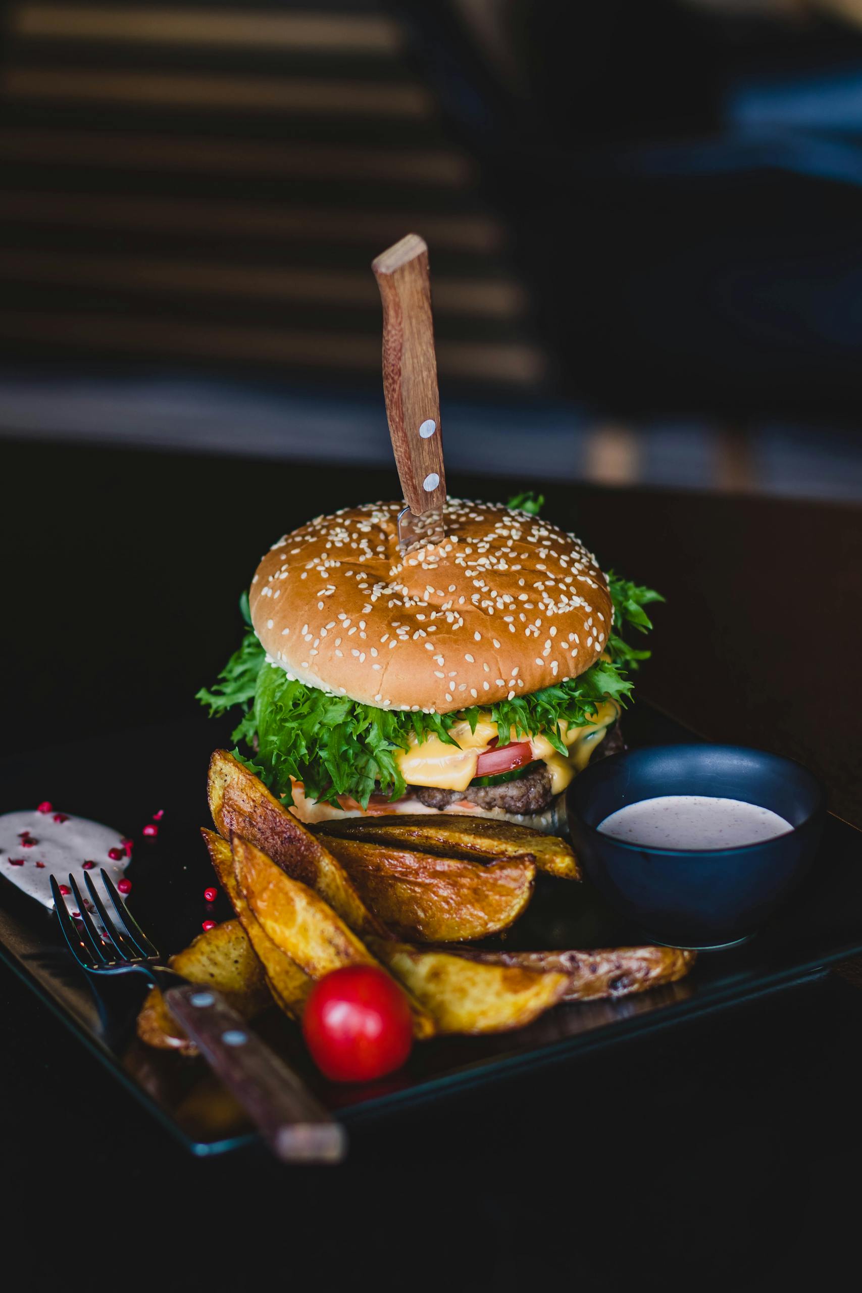 Close-up of a gourmet cheeseburger with wedges and tomato on a black plate. Celebrity restaurants in Atlanta.