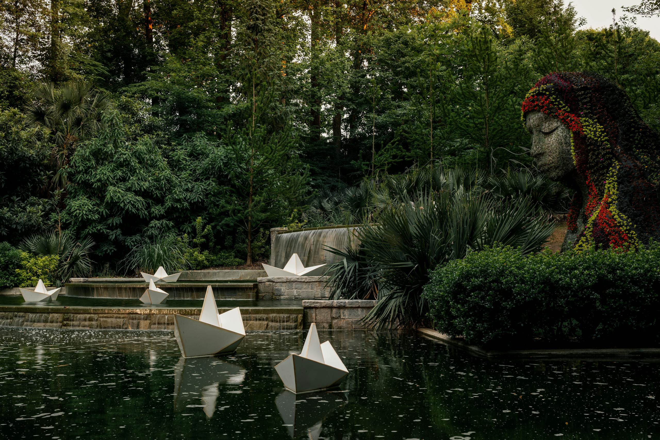 Beautiful garden scene featuring sculpture, paper boats, and lush greenery.